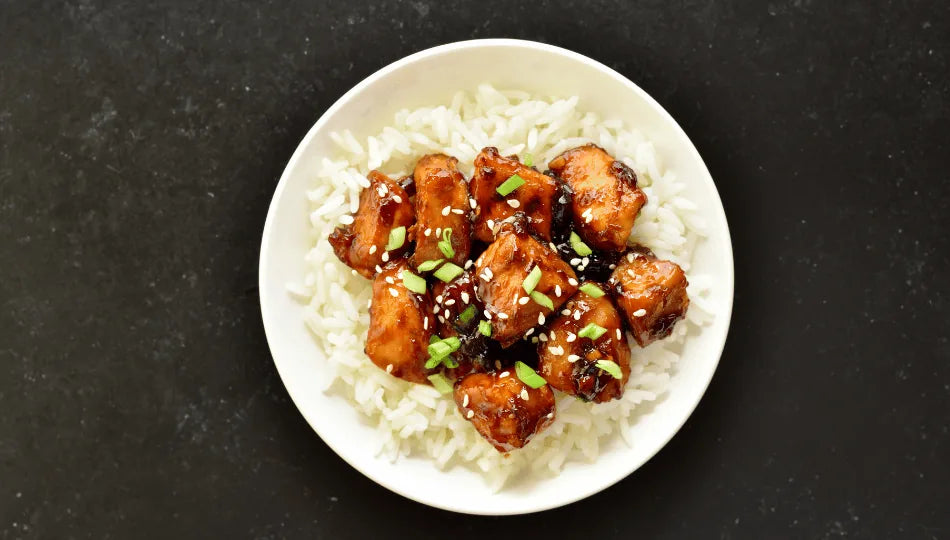 Chicken Teriyaki und Reis auf einem weißen Teller, verfeinert mit Kräutern. 