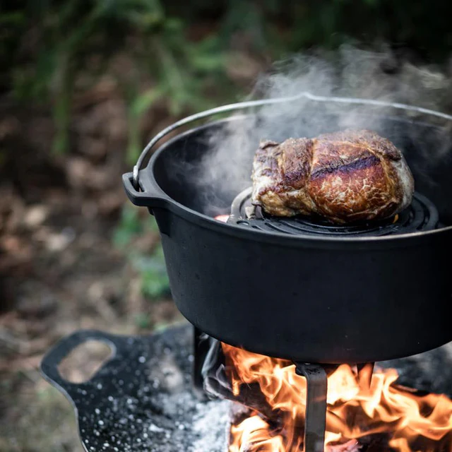 ein großes dampfendes Stück Fleisch in einem Dutch Oven über offenem Feuer auf einer Feuerschale