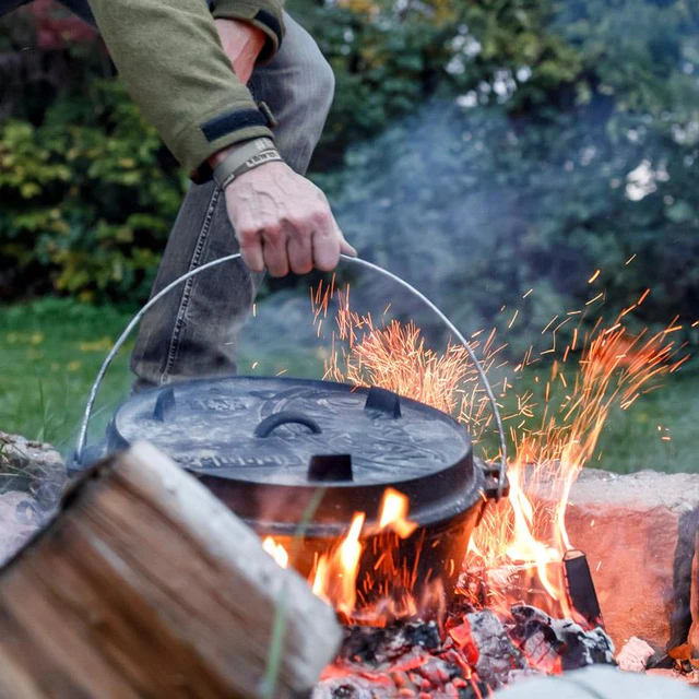 ein großer 12er Feuertopf wird mit dem Henkel in funkensprühendes Feuer gestellt