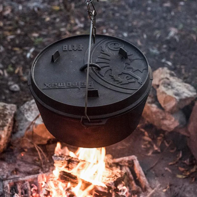 ein schwerer Gusseisentopf hängt an einer Kette über einem Lagerfeuer während der Dämmerung