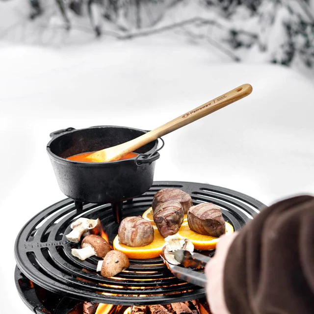 Grillen von Pilzen und Fleisch über offenem Feuer und kochen eines Eintopfs in einem Dutch Oven in einer Schneelandschaft