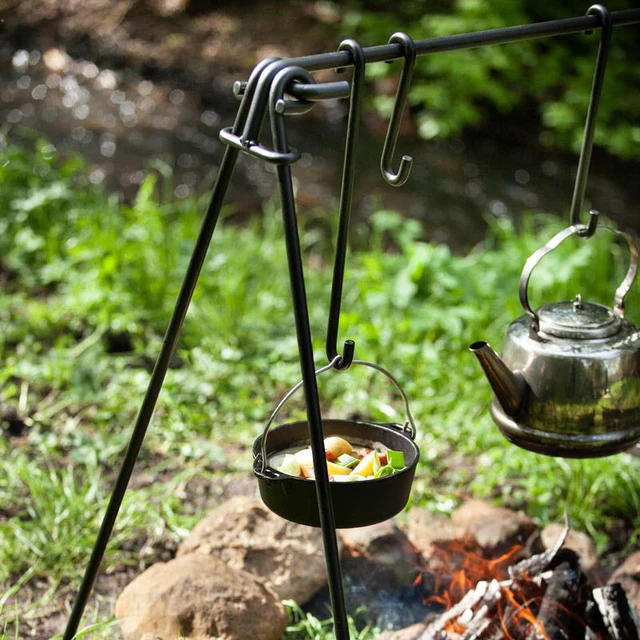 Ein Lagerfeuer über dem eine Suppe in einem Dutch Oven und eine glänzende Teekanne an Haken hängen