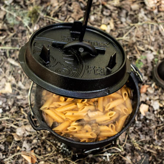 ein dampfendes Nudelgericht im Dutch Oven bei dem der Deckel gerade mit Hilfe eines Deckelhebers genommen wird