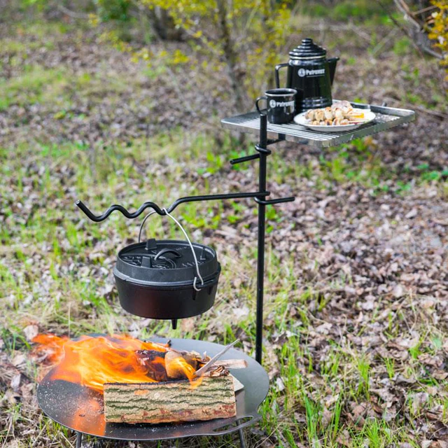 eine Feuerstelle über dem ein Gusstopf hängt und ein Tablet mit einer Kaffeekanne, einer Tasse und einem Teller