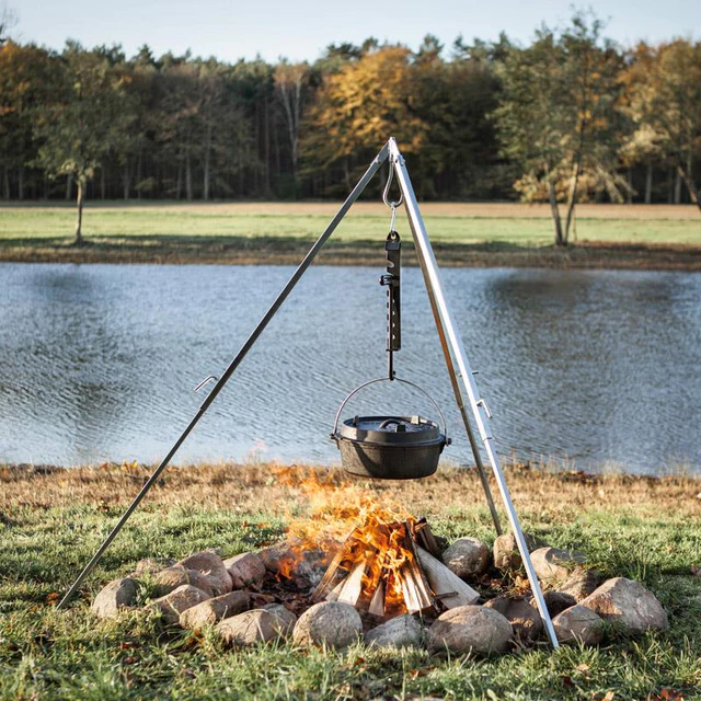 vor einem See hängt an einem Dreibein ein Gusstopf über einem Lagerfeuer