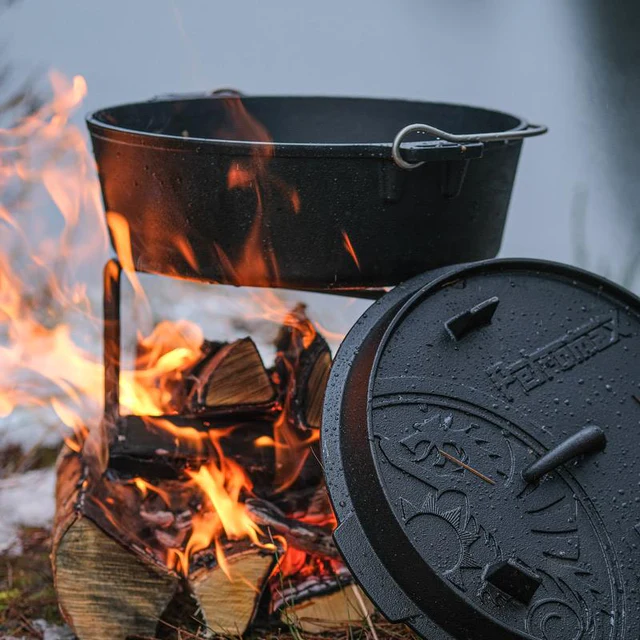 Über brennendem Holz steht ein Feuertopf, dessen Deckel am Dutch Oven anlehnt