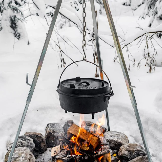 ein Dutch Oven mit Füßen hängt an einem Dreibein über einem Lagerfeuer im tiefen Winter